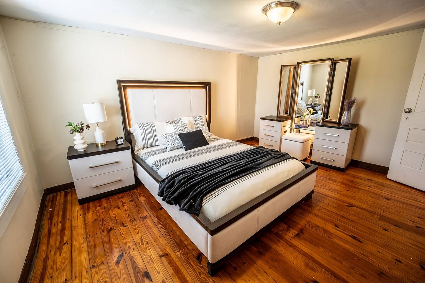 A bedroom with a bed, bedside tables, a dresser, a mirror, and a window with blinds.