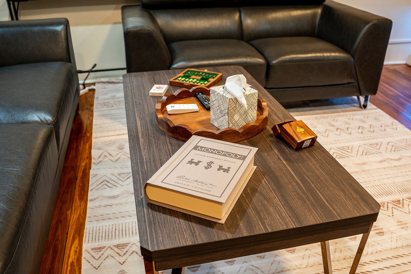 A room with a dark brown wooden coffee table, a Monopoly book, a chess set, and a remote control.