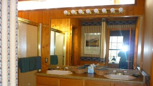 Casa de banho com armários de madeira, duas pias, um espelho e uma janela.