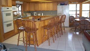 Cozinha com armários de madeira, uma ilha central com banquetas e uma área de refeições com mesa e cadeiras.