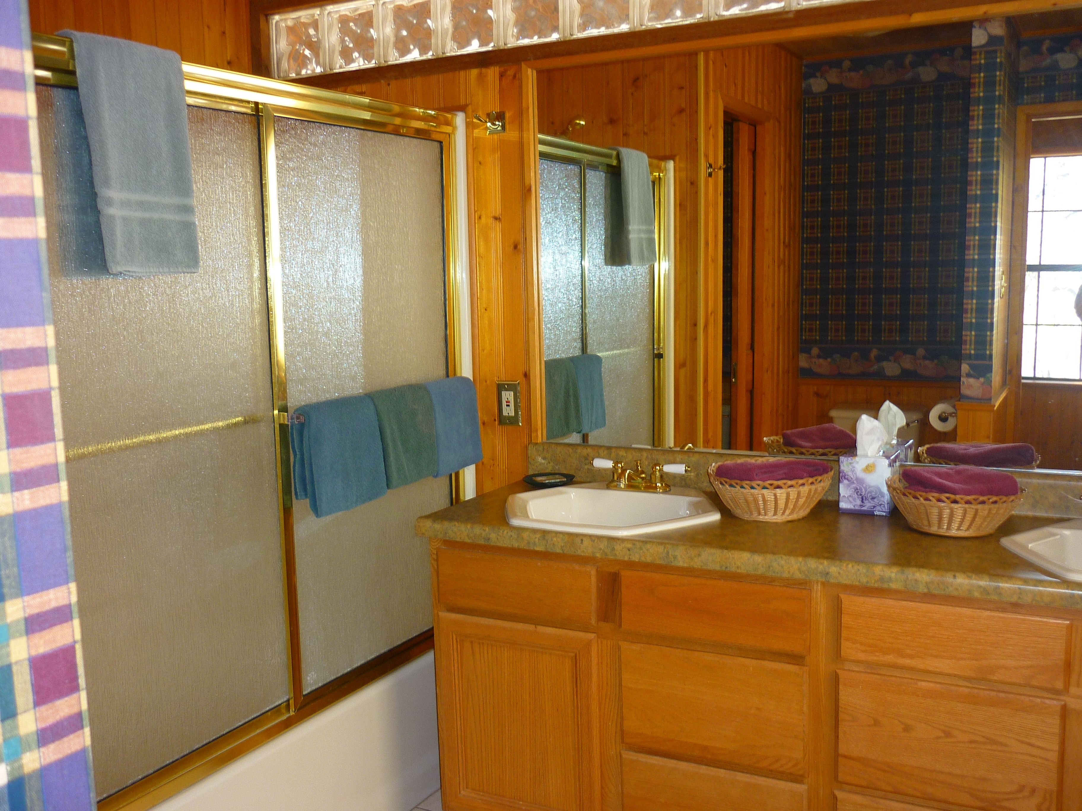 A bathroom with wooden cabinets, a sink, a mirror, and a shower with a glass door.