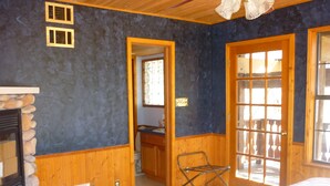 Um quarto com lareira de pedra, paredes de madeira, uma cama com colcha colorida e uma porta que dá para uma área externa.