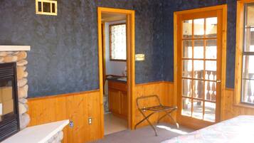 A room with a stone fireplace, wooden walls, a bed with a colorful quilt, and a door leading to an outdoor area.