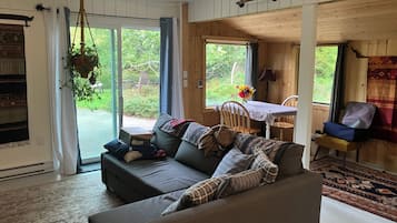 Una sala de estar acogedora con un sofá, una mesa de comedor con sillas y vistas al exterior a través de grandes ventanales.