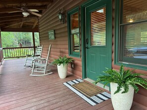A wooden porch with rocking chairs, a green door, and potted plants.