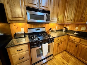 A kitchen with wooden cabinets, a stainless steel stove, a microwave, and a granite countertop.