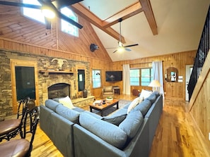 A cozy living room with a stone fireplace, wooden beams, a large sofa, and a television.