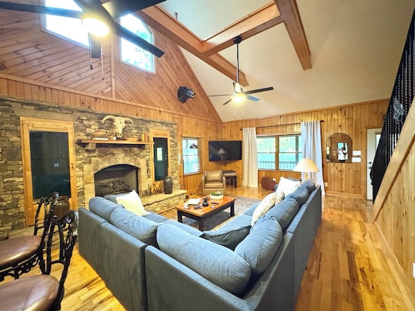 A cozy living room with a stone fireplace, wooden beams, a large sofa, and a television.