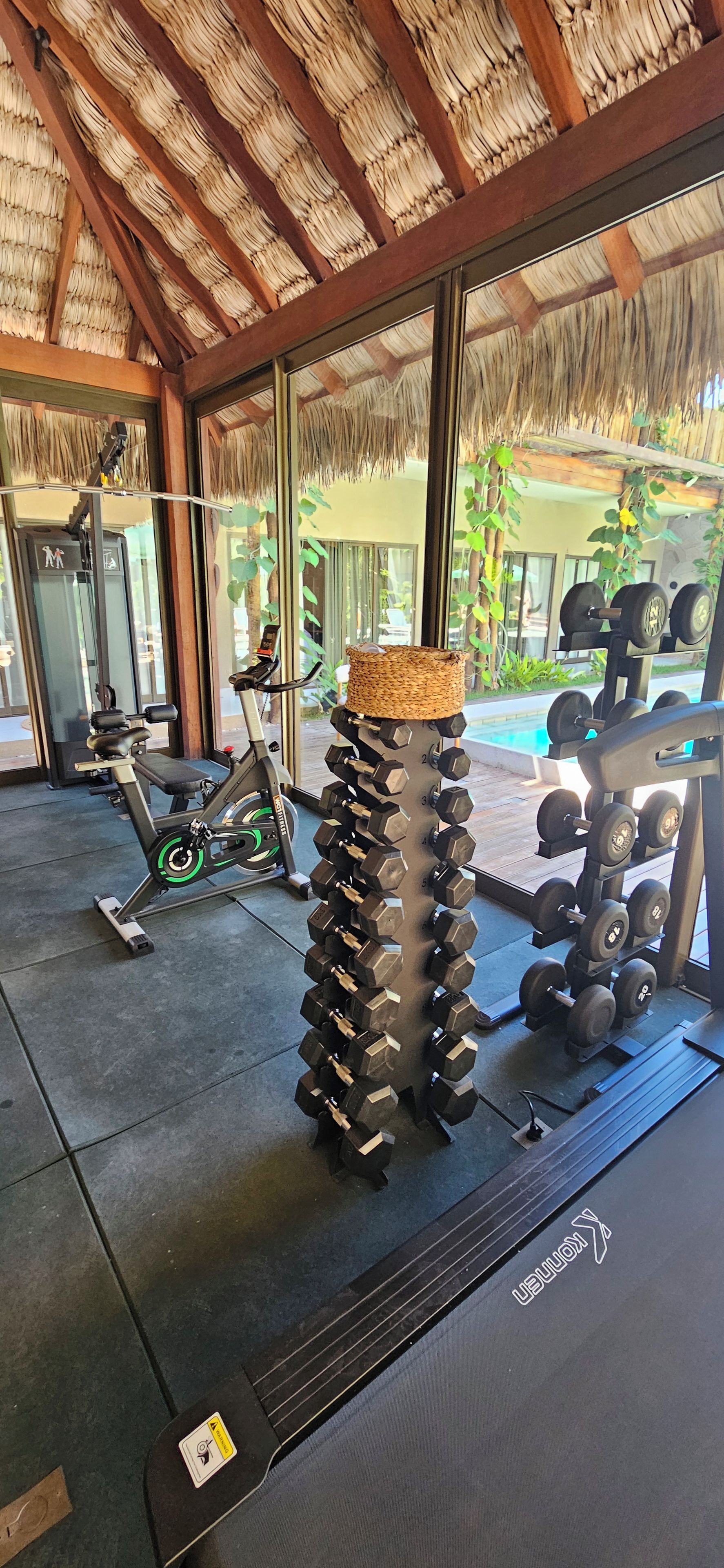 A gym with exercise equipment, including a stationary bike, a bench, and a rack of dumbbells.
