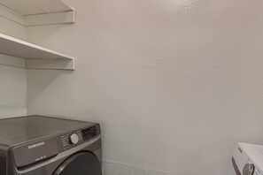 A Samsung washing machine in a laundry area with a white wall and a shelf above it. - Comfy 2-bedroom townhome in East Austin. Huge back yard! (Austin)