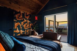 A hotel room with a large bed, a view of the sunset through the balcony, and a Netflix logo on the wall. - Stunning Views | Sauna | 4 Kings | Hot Tub | Golf (Gatlinburg)