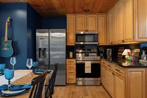 A kitchen with wooden cabinets, stainless steel appliances, and a dining area with a table set for two. - Stunning Views | Sauna | 4 Kings | Hot Tub | Golf (Gatlinburg)