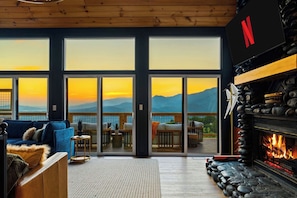 Un salon chaleureux avec une cheminée, un canapé et une vue sur les montagnes, visible à travers de grandes fenêtres.