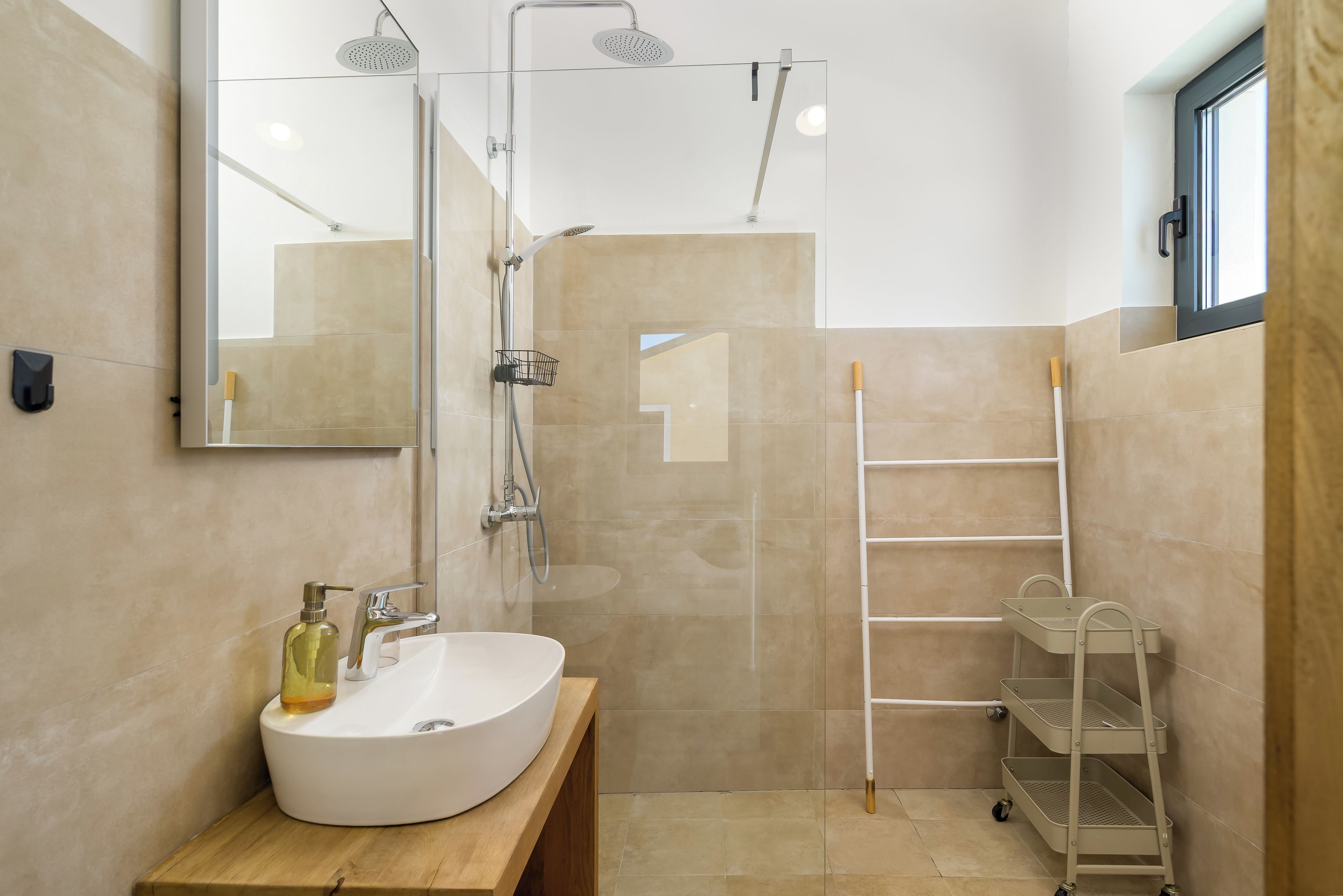 Une salle de bain moderne avec un grand miroir, un lavabo, une douche équipée d’un pommeau de douche à main et une étagère blanche.