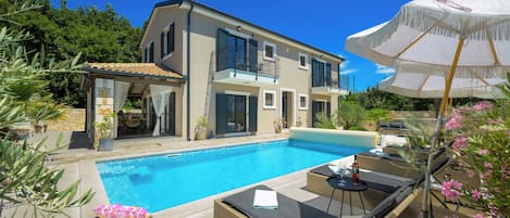 A two-story house with a swimming pool, outdoor furniture, and a pergola.