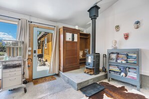 A cozy room with a wood-burning stove, a bookshelf, and a door leading to an outdoor area. - Monthly Rental - Close to Town ~ Mountain Views ~ A/C (Salida)
