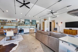 A modern kitchen with a dining area, a large grey sofa, and a flat-screen TV mounted on the wall. - Monthly Rental - Close to Town ~ Mountain Views ~ A/C (Salida)