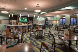 A hotel lobby with a bar area, multiple dining tables and chairs, and a large screen displaying a program. - Luxury 9BR ChampionsGate Retreat Pool, Spa, Game Rooms & Resort Access (Davenport)