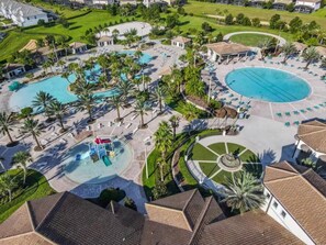 An aerial view of a resort with multiple swimming pools, palm trees, and a central circular area with a fountain. - Luxury 9BR ChampionsGate Retreat Pool, Spa, Game Rooms & Resort Access (Davenport)
