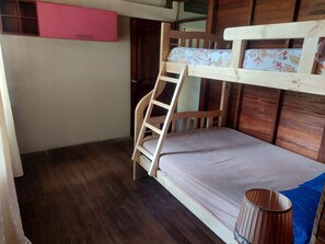 Una cama tipo litera con una escalera, un mueble rosa pequeño y una manta azul en el suelo.