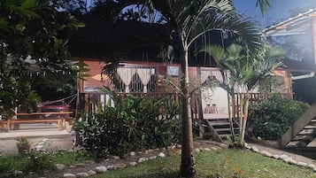 A wooden building with a balcony, surrounded by lush greenery and a palm tree.