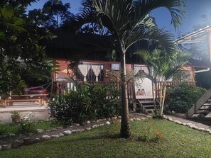A wooden building with a balcony, surrounded by lush greenery and a palm tree.