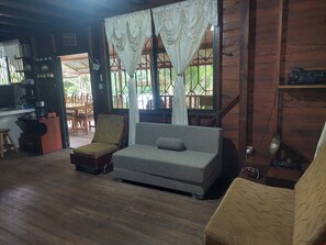 A wooden interior with a sofa, a chair, a small table, and a kitchen area with a coffee machine.