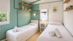 A room with two single beds, a small bedside table with a lamp, and shelves with books and pictures.