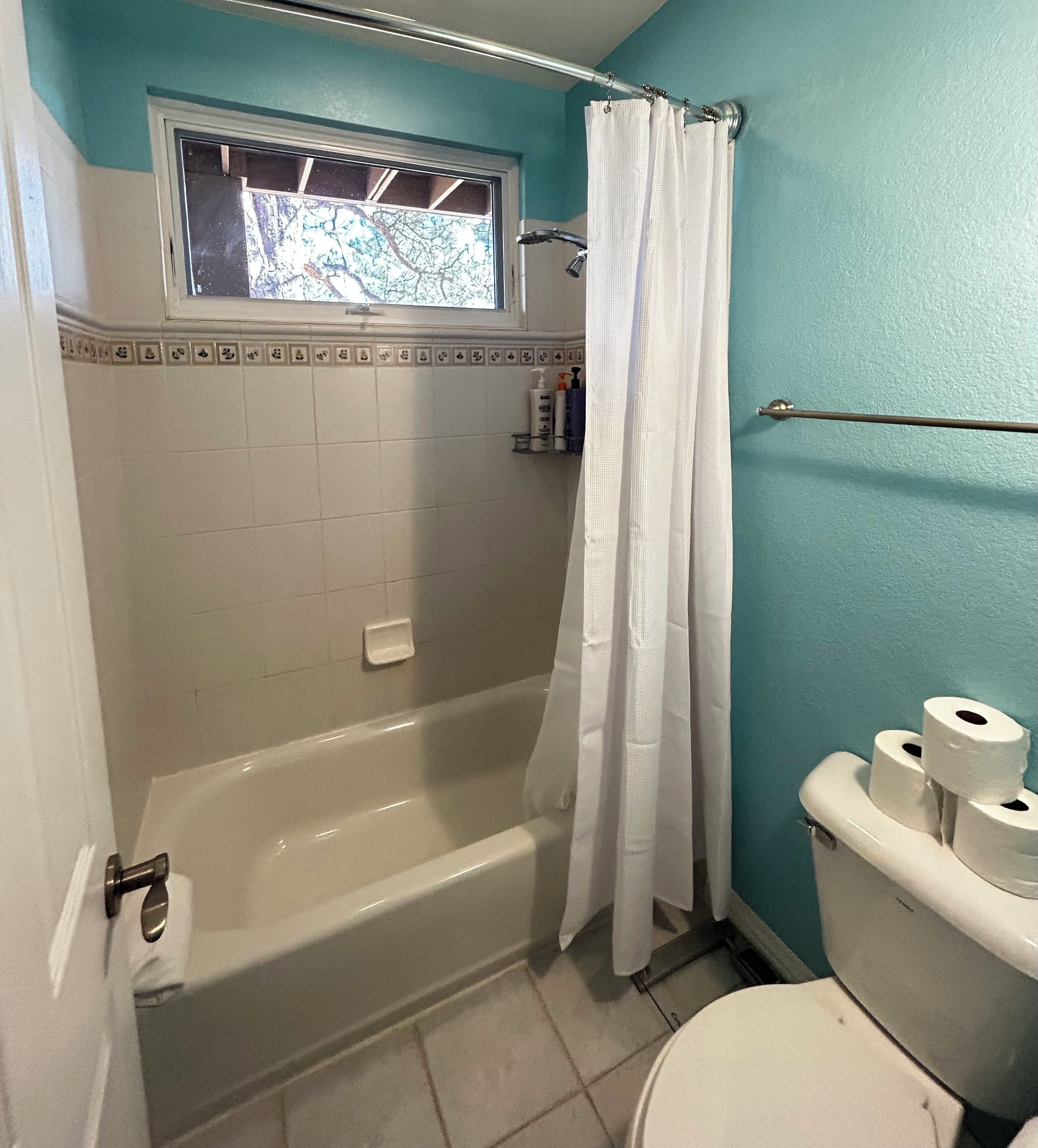 A bathroom with a bathtub, a toilet, and a window above the tub.