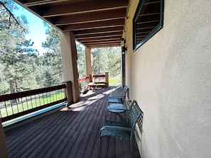 A covered outdoor area with wooden flooring, metal chairs, and a bench. - Ponderosa Pine Getaway in the Boulder Foothills (Boulder)
