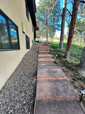 A pathway leading to a building with a beige exterior, surrounded by trees and gravel. - Ponderosa Pine Getaway in the Boulder Foothills (Boulder)