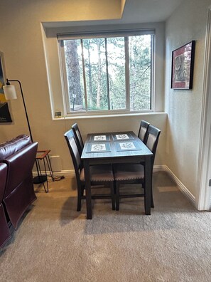 A dining area with a table and chairs, a window with a view of trees, and a lamp on the left. - Ponderosa Pine Getaway in the Boulder Foothills (Boulder)