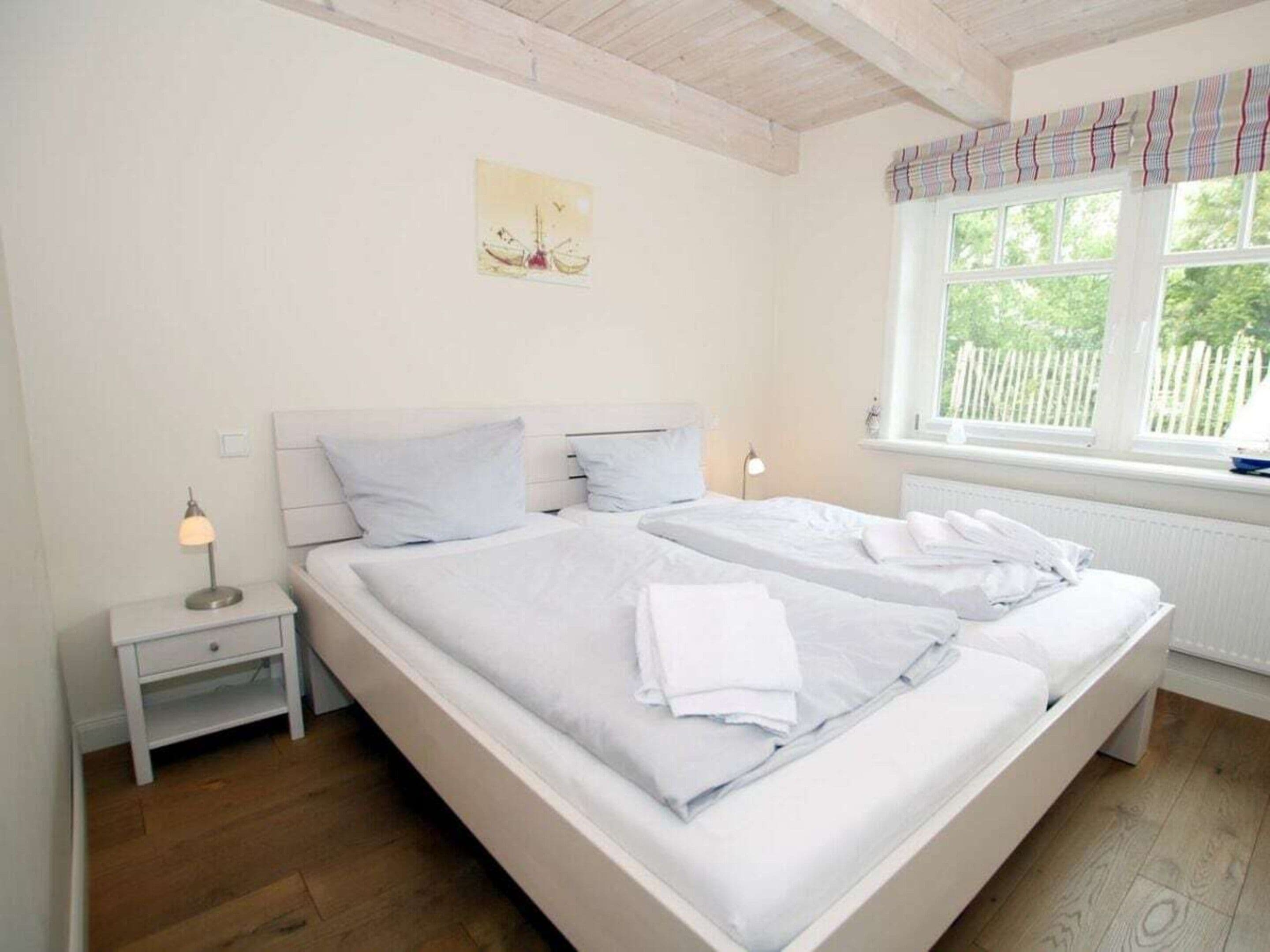 A bedroom with a large bed, bedside tables, a window with curtains, and a painting on the wall.
