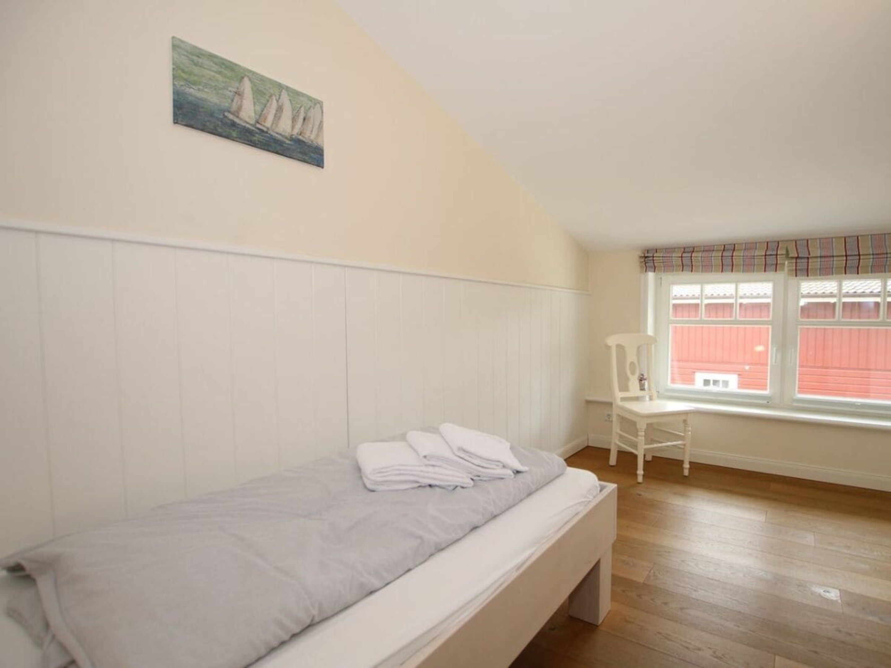 A bedroom with a single bed, a chair, a window with curtains, and a painting on the wall.