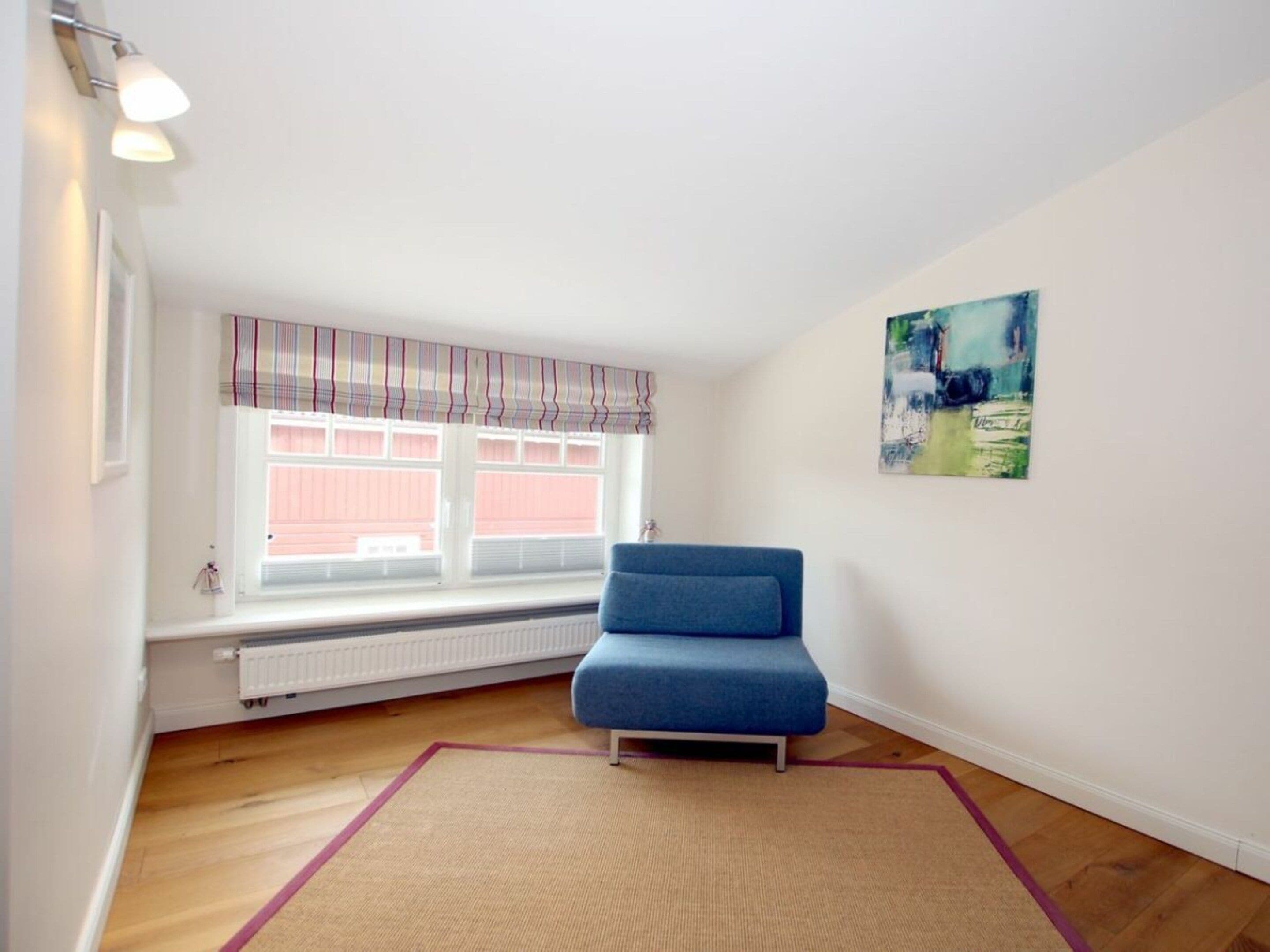 Une pièce avec un canapé bleu, une fenêtre avec des rideaux à rayures, un radiateur et un tableau accroché au mur.