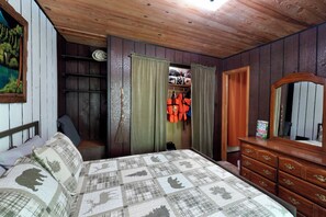 A bedroom with a wooden ceiling, a bed with patterned bedding, a dresser, a mirror, and a closet with hanging clothes and a broom. - Entire house located on the Shenandoah River (Harpers Ferry)