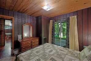 Een slaapkamer met een houten plafond, een dressoir, een bed met sprei en een raam met gordijnen.