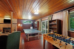 Ein Raum mit einem Tischtennisch, einem Kicker, einem Kamin aus Ziegelsteinen und einem an der Wand befestigten Fernseher.