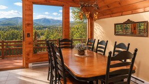 A wooden dining room with a large table and chairs, a hanging light fixture, and a view of mountains through large windows. - Luxury Lodge for 2–4 • Gore Views , AC, Pets (North Creek)