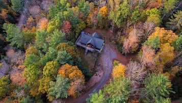 Eine Vogelperspektive zeigt eine Hütte, umgeben von dichtem Wald, mit einem gewundenen Pfad, der dorthin führt.