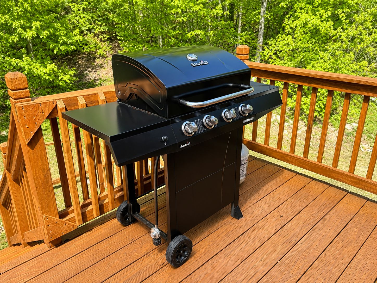 Una parrilla portátil de carbón sobre una terraza de madera con barandilla.