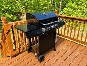 A portable charcoal grill on a wooden deck with a railing.