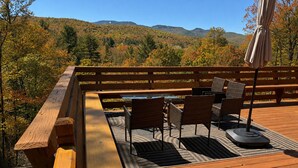An outdoor wooden deck with a table and chairs, surrounded by a wooden railing. - Luxury Lodge for 2–4 • Gore Views , AC, Pets (North Creek)