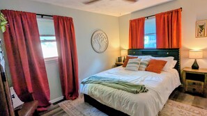 A bedroom with a bed, two bedside tables, a nightstand, a wall clock, and a window with curtains. - Delightful 2-bedroom house with an office, deck and fire pit in Sioux Falls (Sioux Falls)