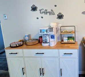 A kitchenette with a coffee machine, tea and sugar containers, a tray of cookies, and a shelf with tea bags. - Delightful 2-bedroom house with an office, deck and fire pit in Sioux Falls (Sioux Falls)