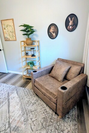 A room with a brown sofa, a wooden shelf with decorative items, a map on the wall, and a patterned rug. - Delightful 2-bedroom house with an office, deck and fire pit in Sioux Falls (Sioux Falls)