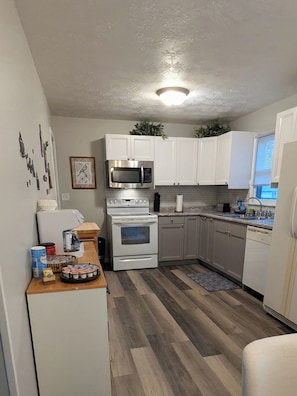 A compact kitchen with white cabinets, a microwave, an oven, and a sink. - Delightful 2-bedroom house with an office, deck and fire pit in Sioux Falls (Sioux Falls)