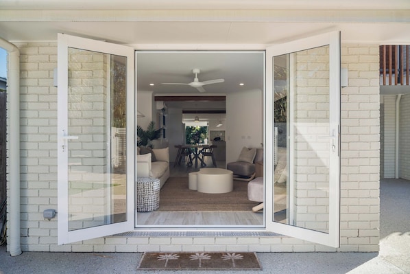 A modern house with a glass door entrance, a dining area, and a living room with sofas and a coffee table.