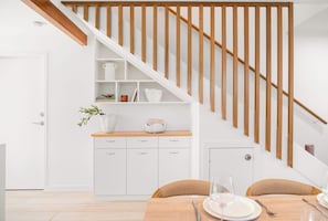 A modern kitchen with white cabinetry, a wooden staircase, and a dining area with a table set for two.