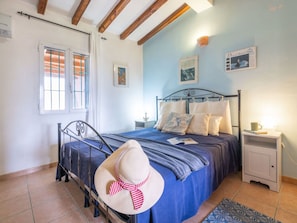 Un dormitorio con estructura de cama metálica, colcha azul y pared blanca con un cuadro enmarcado.